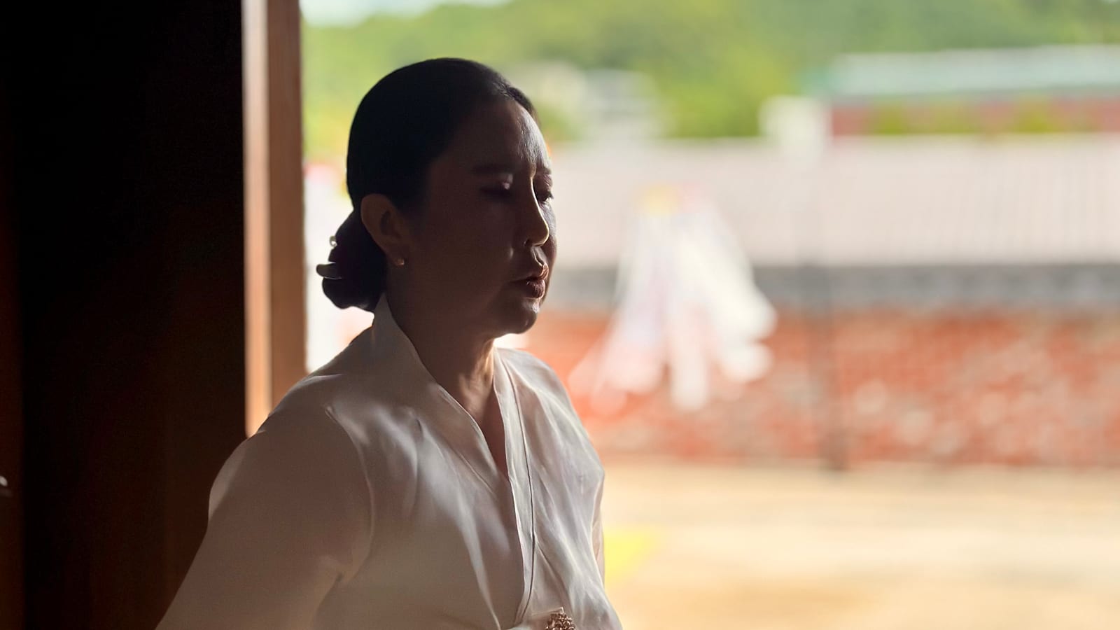 한옥 문간에 선 당주보살, 흰 한복 차림의 옆모습