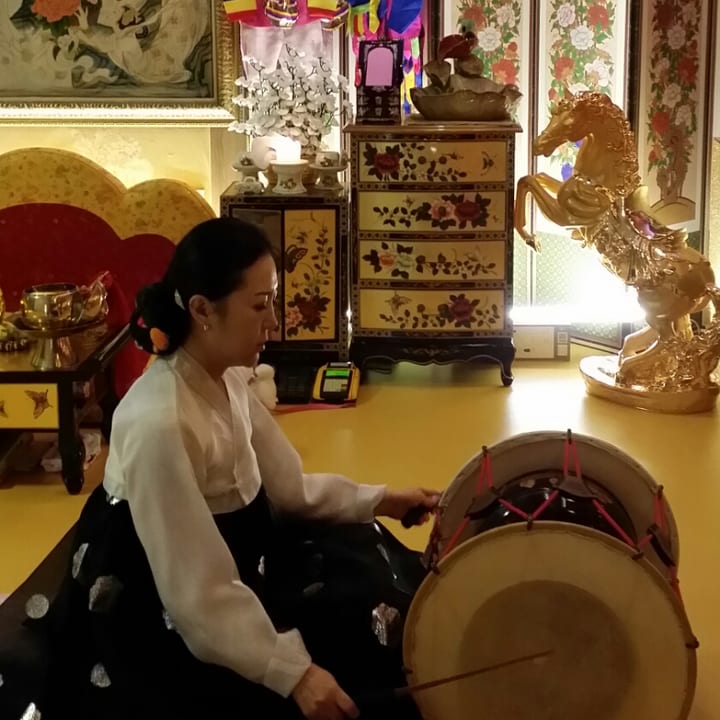 병풍과 자개장이 놓인 신당에서 장구를 치는 대표